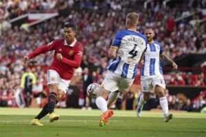 emain Manchester United Cristiano Ronaldo, kiri, menendang bola ketika pemain Brighton Adam Webster mencoba menghentikannya selama pertandingan sepak bola Liga Premier Inggris antara Manchester United dan Brighton di stadion Old Trafford di Manchester, Inggris, Ahad, 7 Agustus 2022.