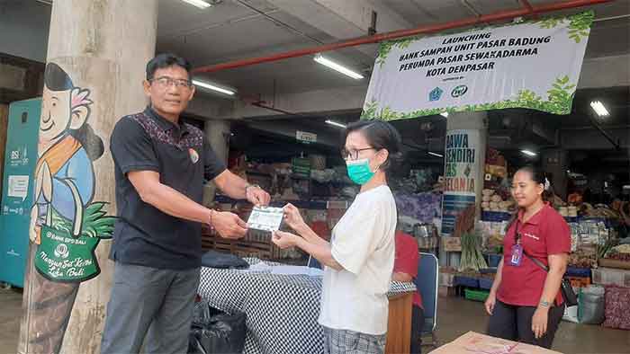 Kelapa Bagian Kebersihan dan Keamanan Perumda Pasar Sewakadarma I Nyoman Swastika meyerahkan buku tabungan kepada penabung sampah di Pasar Badung. (Foto: M-011)
