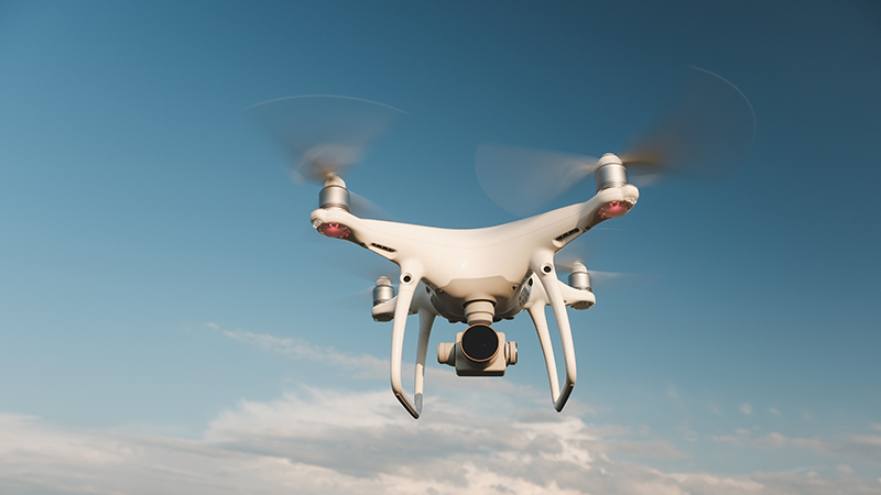 White drone hovering in a bright blue sky