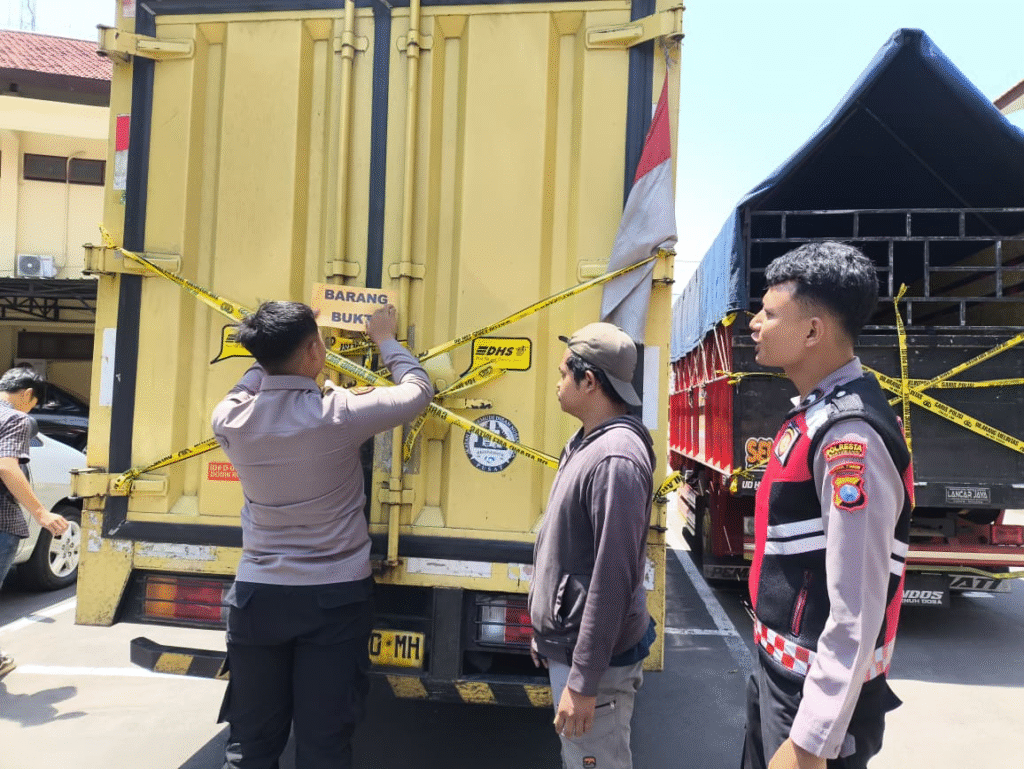 Petugas Polresta Banyuwangi saat memasang garis polisi dan label barang bukti pada truk box bermuatan ribuan botol arak ilegal yang diamankan di kawasan Kalipuro.