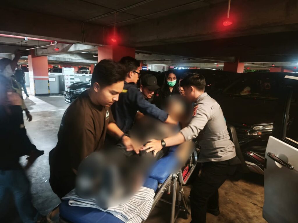 Petugas kepolisian bersama tim medis mengevakuasi seorang pria yang ditemukan meninggal di dalam mobil di area parkir Terminal Kedatangan Internasional Bandara I Gusti Ngurah Rai, Minggu (19/10/2025) malam.