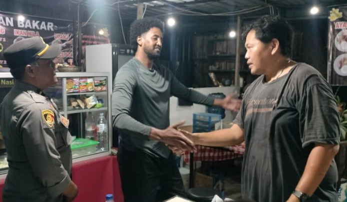 Turis asal Somalia berjabat tangan dengan sopir taksi online usai menyelesaikan kesalahpahaman terkait dugaan pencurian ponsel, disaksikan petugas Polsek Denpasar Timur, Senin (4/11/2025) malam.