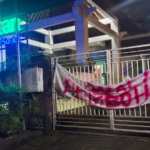 Spanduk bernada protes terpasang di gerbang Kantor BPJS Kesehatan Cabang Denpasar, Sabtu (21/2/2026) malam.