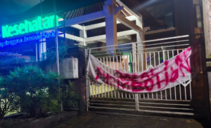 Spanduk bernada protes terpasang di gerbang Kantor BPJS Kesehatan Cabang Denpasar, Sabtu (21/2/2026) malam.