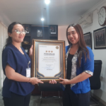 Bagian Mutu Layanan Kesehatan BPJS Kesehatan Kantor Cabang Denpasar, I Kadek Astiti Muliantari (kiri), menyerahkan piagam penghargaan kepada Penanggung Jawab Klinik Anugerah Denpasar, dr. Ida Ayu Gde Deviantari Utari Manuaba, S.Ket.