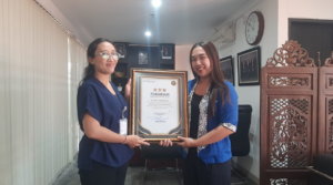 Bagian Mutu Layanan Kesehatan BPJS Kesehatan Kantor Cabang Denpasar, I Kadek Astiti Muliantari (kiri), menyerahkan piagam penghargaan kepada Penanggung Jawab Klinik Anugerah Denpasar, dr. Ida Ayu Gde Deviantari Utari Manuaba, S.Ket.