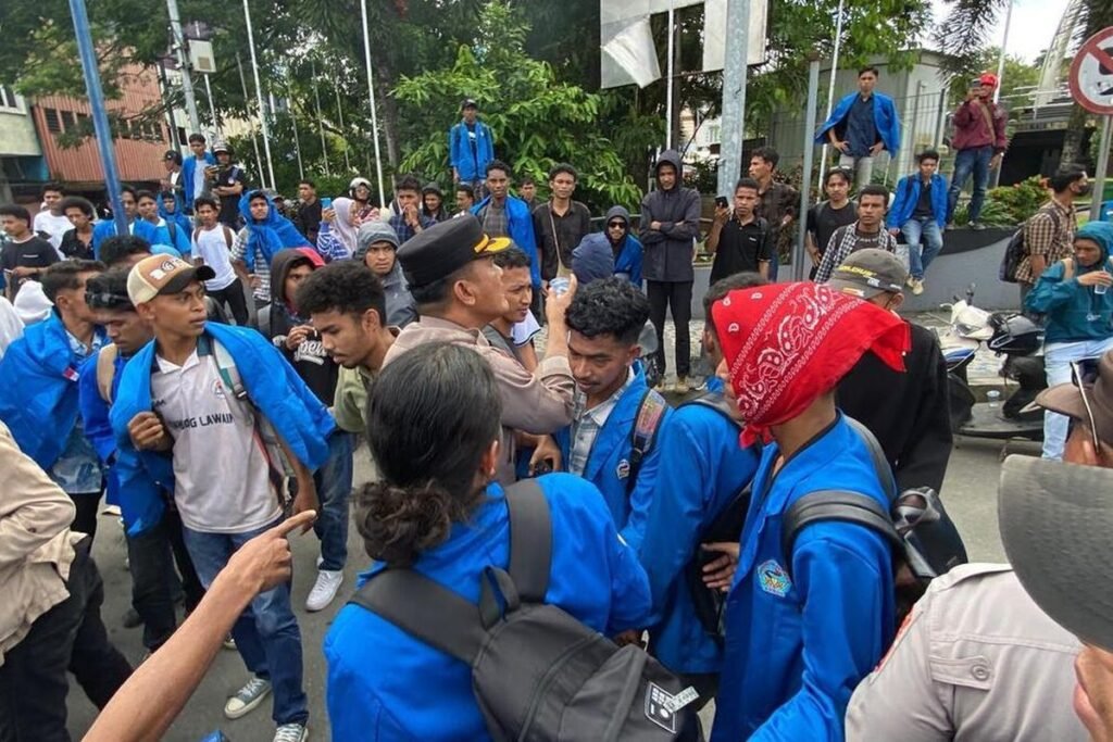 AMBON, MENITINI - Aksi unjuk rasa yang dilakukan oleh ratusan mahasiswa di Kota Ambon berujung ricuh pada, Rabu (17/6/2026). Demonstrasi yang awalnya berlangsung damai tersebut berubah menjadi bentrokan antara massa aksi dan aparat kepolisian di kawasan, Gong Perdamaian, pusat kota Ambon. Para mahasiswa yang tergabung dalam berbagai organisasi kampus itu turun ke jalan untuk menyampaikan aspirasi terkait sejumlah isu daerah dan nasional. Mereka memulai aksi dengan long march sambil membawa spanduk dan menyuarakan tuntutan melalui pengeras suara. Situasi mulai memanas ketika massa mencoba menerobos barikade polisi yang berjaga di sekitar lokasi aksi. Aparat yang berusaha menghalau massa mendapat perlawanan, sehingga terjadi aksi saling dorong yang kemudian berkembang menjadi adu jotos antara beberapa pendemo dan petugas Kericuhan bermula ketika mahasiswa membakar ban bekas di badan jalan saat aksi berlangsung. “Kami menuntut peninjauan kembali hingga pembatalan atas seluruh produk kebijakan publik yang dinilai kontradiktif dengan asas kemaslahatan rakyat serta mengabaikan prinsip-prinsip good governance,” teriak Koordinator Aksi Eston Halamury saat menyampaikan orasi. Menurut informasi yang dihimpun, aksi yang semula berlangsung tertib berubah memanas ketika polisi berupaya memadamkan ban bekas yang dibakar karena dinilai mengganggu kelancaran arus lalu lintas. Upaya tersebut mendapat penolakan dari massa aksi hingga memicu bentrokan antara mahasiswa dan aparat kepolisian. Mahasiswa dan Polisi Saling Serang Dalam kericuhan itu, ratusan mahasiswa dari berbagai perguruan tinggi di Ambon terlibat aksi saling dorong dan adu jotos dengan aparat. Sejumlah mahasiswa dilaporkan mengalami luka memar akibat bentrokan tersebut. Beberapa peserta aksi yang diamankan polisi sempat dibawa ke Polsek Sirimau yang berada tidak jauh dari lokasi demonstrasi. Situasi semakin memanas setelah sebagian mahasiswa melempari aparat dengan batu sebagai bentuk protes atas tindakan yang mereka anggap represif. Aksi kejar-kejaran antara polisi dan mahasiswa pun tidak dapat dihindari. Dalam insiden tersebut, seorang anggota polisi dilaporkan terluka akibat terkena lemparan batu. Kericuhan akhirnya mereda setelah Kapolresta Pulau Ambon dan Pulau-Pulau Lease Kombes Pol Yoga Putra Prima Setya turun langsung ke lokasi untuk menenangkan anggotanya dan massa aksi. Mahasiswa pendemo sempat diamankan kemudian dilepaskan kembali. Aparat kepolisian akhirnya mengambil langkah untuk membubarkan massa dan mengendalikan situasi. Beberapa mahasiswa terlihat diamankan, sementara sejumlah lainnya mengalami luka ringan akibat bentrokan tersebut. Hingga berita ini diturunkan, kondisi di lokasi aksi sudah berangsur kondusif. Pihak kepolisian mengimbau agar mahasiswa dapat menyampaikan aspirasi secara tertib dan damai, sementara perwakilan mahasiswa menyatakan akan tetap mengawal tuntutan mereka melalui jalur yang konstitusional. (M-009).