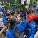AMBON, MENITINI - Aksi unjuk rasa yang dilakukan oleh ratusan mahasiswa di Kota Ambon berujung ricuh pada, Rabu (17/6/2026). Demonstrasi yang awalnya berlangsung damai tersebut berubah menjadi bentrokan antara massa aksi dan aparat kepolisian di kawasan, Gong Perdamaian, pusat kota Ambon. Para mahasiswa yang tergabung dalam berbagai organisasi kampus itu turun ke jalan untuk menyampaikan aspirasi terkait sejumlah isu daerah dan nasional. Mereka memulai aksi dengan long march sambil membawa spanduk dan menyuarakan tuntutan melalui pengeras suara. Situasi mulai memanas ketika massa mencoba menerobos barikade polisi yang berjaga di sekitar lokasi aksi. Aparat yang berusaha menghalau massa mendapat perlawanan, sehingga terjadi aksi saling dorong yang kemudian berkembang menjadi adu jotos antara beberapa pendemo dan petugas Kericuhan bermula ketika mahasiswa membakar ban bekas di badan jalan saat aksi berlangsung. “Kami menuntut peninjauan kembali hingga pembatalan atas seluruh produk kebijakan publik yang dinilai kontradiktif dengan asas kemaslahatan rakyat serta mengabaikan prinsip-prinsip good governance,” teriak Koordinator Aksi Eston Halamury saat menyampaikan orasi. Menurut informasi yang dihimpun, aksi yang semula berlangsung tertib berubah memanas ketika polisi berupaya memadamkan ban bekas yang dibakar karena dinilai mengganggu kelancaran arus lalu lintas. Upaya tersebut mendapat penolakan dari massa aksi hingga memicu bentrokan antara mahasiswa dan aparat kepolisian. Mahasiswa dan Polisi Saling Serang Dalam kericuhan itu, ratusan mahasiswa dari berbagai perguruan tinggi di Ambon terlibat aksi saling dorong dan adu jotos dengan aparat. Sejumlah mahasiswa dilaporkan mengalami luka memar akibat bentrokan tersebut. Beberapa peserta aksi yang diamankan polisi sempat dibawa ke Polsek Sirimau yang berada tidak jauh dari lokasi demonstrasi. Situasi semakin memanas setelah sebagian mahasiswa melempari aparat dengan batu sebagai bentuk protes atas tindakan yang mereka anggap represif. Aksi kejar-kejaran antara polisi dan mahasiswa pun tidak dapat dihindari. Dalam insiden tersebut, seorang anggota polisi dilaporkan terluka akibat terkena lemparan batu. Kericuhan akhirnya mereda setelah Kapolresta Pulau Ambon dan Pulau-Pulau Lease Kombes Pol Yoga Putra Prima Setya turun langsung ke lokasi untuk menenangkan anggotanya dan massa aksi. Mahasiswa pendemo sempat diamankan kemudian dilepaskan kembali. Aparat kepolisian akhirnya mengambil langkah untuk membubarkan massa dan mengendalikan situasi. Beberapa mahasiswa terlihat diamankan, sementara sejumlah lainnya mengalami luka ringan akibat bentrokan tersebut. Hingga berita ini diturunkan, kondisi di lokasi aksi sudah berangsur kondusif. Pihak kepolisian mengimbau agar mahasiswa dapat menyampaikan aspirasi secara tertib dan damai, sementara perwakilan mahasiswa menyatakan akan tetap mengawal tuntutan mereka melalui jalur yang konstitusional. (M-009).