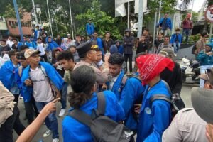 AMBON, MENITINI - Aksi unjuk rasa yang dilakukan oleh ratusan mahasiswa di Kota Ambon berujung ricuh pada, Rabu (17/6/2026). Demonstrasi yang awalnya berlangsung damai tersebut berubah menjadi bentrokan antara massa aksi dan aparat kepolisian di kawasan, Gong Perdamaian, pusat kota Ambon. Para mahasiswa yang tergabung dalam berbagai organisasi kampus itu turun ke jalan untuk menyampaikan aspirasi terkait sejumlah isu daerah dan nasional. Mereka memulai aksi dengan long march sambil membawa spanduk dan menyuarakan tuntutan melalui pengeras suara. Situasi mulai memanas ketika massa mencoba menerobos barikade polisi yang berjaga di sekitar lokasi aksi. Aparat yang berusaha menghalau massa mendapat perlawanan, sehingga terjadi aksi saling dorong yang kemudian berkembang menjadi adu jotos antara beberapa pendemo dan petugas Kericuhan bermula ketika mahasiswa membakar ban bekas di badan jalan saat aksi berlangsung. “Kami menuntut peninjauan kembali hingga pembatalan atas seluruh produk kebijakan publik yang dinilai kontradiktif dengan asas kemaslahatan rakyat serta mengabaikan prinsip-prinsip good governance,” teriak Koordinator Aksi Eston Halamury saat menyampaikan orasi. Menurut informasi yang dihimpun, aksi yang semula berlangsung tertib berubah memanas ketika polisi berupaya memadamkan ban bekas yang dibakar karena dinilai mengganggu kelancaran arus lalu lintas. Upaya tersebut mendapat penolakan dari massa aksi hingga memicu bentrokan antara mahasiswa dan aparat kepolisian. Mahasiswa dan Polisi Saling Serang Dalam kericuhan itu, ratusan mahasiswa dari berbagai perguruan tinggi di Ambon terlibat aksi saling dorong dan adu jotos dengan aparat. Sejumlah mahasiswa dilaporkan mengalami luka memar akibat bentrokan tersebut. Beberapa peserta aksi yang diamankan polisi sempat dibawa ke Polsek Sirimau yang berada tidak jauh dari lokasi demonstrasi. Situasi semakin memanas setelah sebagian mahasiswa melempari aparat dengan batu sebagai bentuk protes atas tindakan yang mereka anggap represif. Aksi kejar-kejaran antara polisi dan mahasiswa pun tidak dapat dihindari. Dalam insiden tersebut, seorang anggota polisi dilaporkan terluka akibat terkena lemparan batu. Kericuhan akhirnya mereda setelah Kapolresta Pulau Ambon dan Pulau-Pulau Lease Kombes Pol Yoga Putra Prima Setya turun langsung ke lokasi untuk menenangkan anggotanya dan massa aksi. Mahasiswa pendemo sempat diamankan kemudian dilepaskan kembali. Aparat kepolisian akhirnya mengambil langkah untuk membubarkan massa dan mengendalikan situasi. Beberapa mahasiswa terlihat diamankan, sementara sejumlah lainnya mengalami luka ringan akibat bentrokan tersebut. Hingga berita ini diturunkan, kondisi di lokasi aksi sudah berangsur kondusif. Pihak kepolisian mengimbau agar mahasiswa dapat menyampaikan aspirasi secara tertib dan damai, sementara perwakilan mahasiswa menyatakan akan tetap mengawal tuntutan mereka melalui jalur yang konstitusional. (M-009).